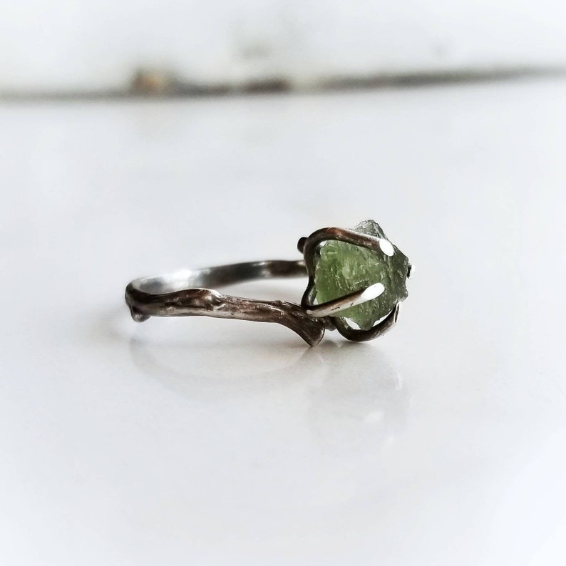 May include: A silver ring with a branch design and a green gemstone set in the center.