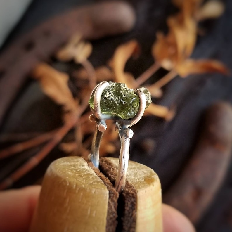 May include: A silver ring with a green peridot gemstone. The ring is set in a simple, modern style and is perfect for everyday wear.