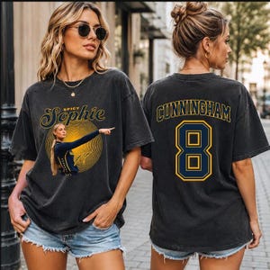 May include: A charcoal gray short-sleeve t-shirt featuring a graphic on the front with the text Spicy Sophie and an illustration of a basketball player. The back of the shirt displays the name CUNNINGHAM and the number 8 in yellow and blue.