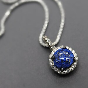 May include: A silver chain necklace with a blue gemstone pendant surrounded by smaller clear gemstones.