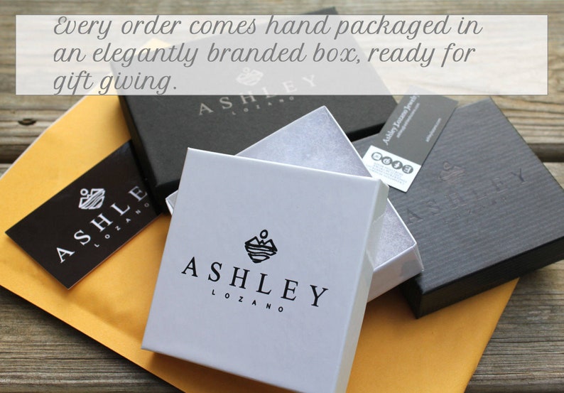 Op de afbeelding: Drie zwarte en witte cadeaudozen met het logo "Ashley Lozano" erop gedrukt. De dozen zijn op elkaar gestapeld en klaar om cadeau te geven.