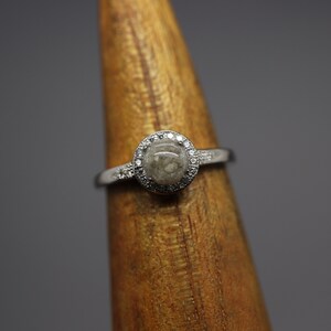 May include: A silver ring featuring a round, grey stone set in a halo of small diamonds.
