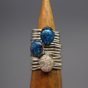Op de afbeelding: Drie zilveren ringen met opaalstenen. De stenen zijn blauw, groen en wit met iriserende glitter.