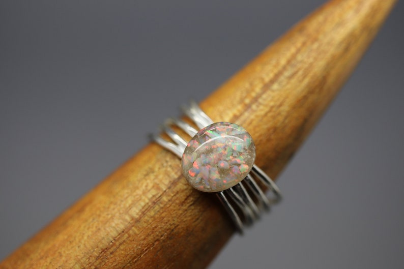 Op de afbeelding: Een zilveren ring met een ronde, iriserende opaal-steen in het midden. De ring is gemaakt van meerdere dunne zilveren banden.