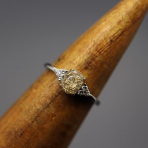 May include: A silver ring with a clear stone set in the center. The stone is filled with small pieces of gold leaf. The ring is set on a wooden display stand.