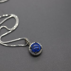 May include: A silver chain necklace with a pendant featuring a round blue gemstone surrounded by smaller clear gemstones.