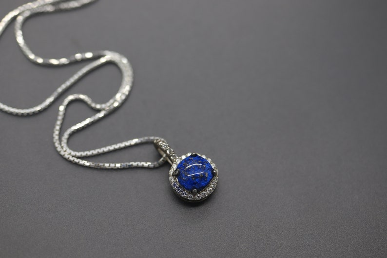 May include: A silver chain necklace with a pendant featuring a round blue gemstone surrounded by smaller clear gemstones.