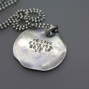 Op de afbeelding: Zilveren ketting met een ronde hanger met de tekst "We leven voor altijd. Beide van ons."