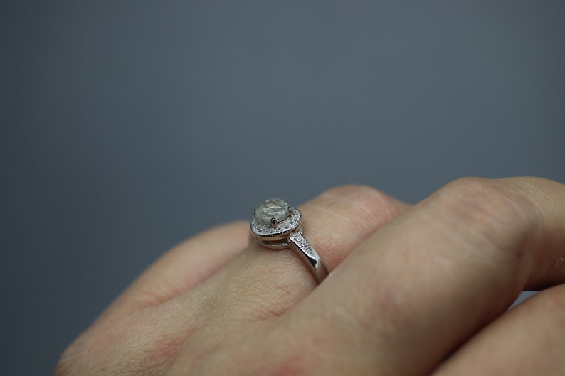 May include: A silver ring featuring a large, clear, oval-shaped gemstone encircled by a halo of smaller gemstones.