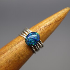 Op de afbeelding: Een zilveren ring met een ovale, blauw-groene steen in het midden.
