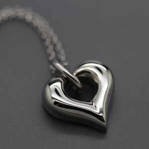 May include: A silver heart-shaped pendant necklace with a smooth, polished finish. The pendant has a large open circle in the centre.