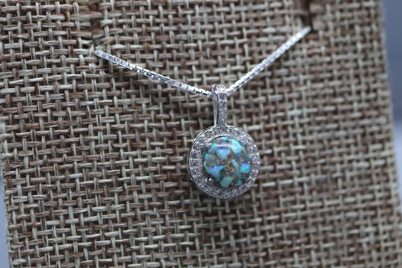 May include: A silver chain necklace with a round pendant featuring a blue and green iridescent stone surrounded by a halo of small clear stones.