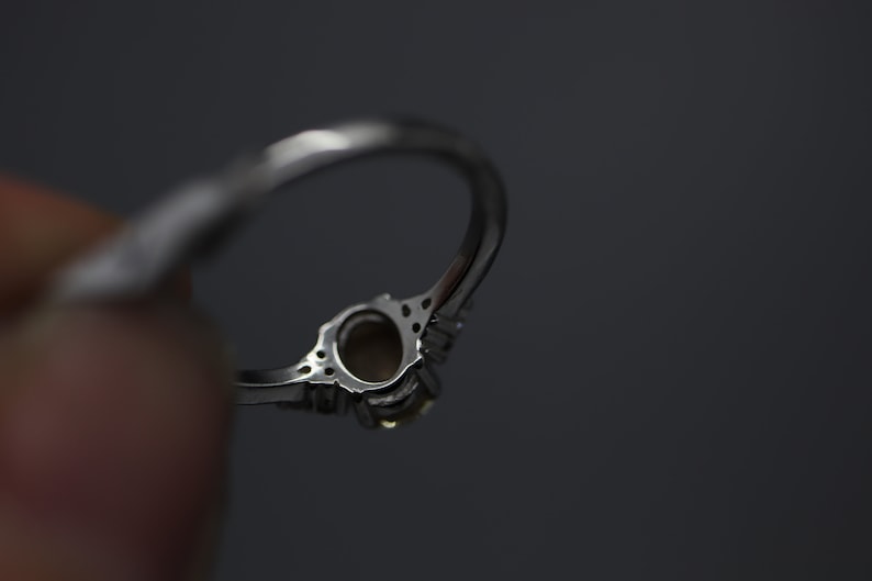 May include: A silver ring with a clear oval-shaped gemstone surrounded by smaller clear gemstones.