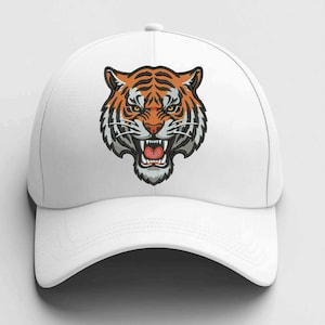 Op de afbeelding: Witte baseballcap met een geborduurde tijgerkop. De tijger is oranje, zwart en wit, met een open mond die tanden laat zien. De cap heeft een gebogen klep en een knoop aan de bovenkant.