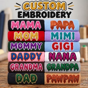 Puede incluir: Una pila de sudaderas dobladas con bordado personalizado y el texto CUSTOM EMBROIDERY en la parte superior. Cada sudadera muestra un título familiar diferente en una fuente brillante y goteante, incluyendo MAMA, PAPA, MOM, MIMI, MOMMY, GIGI, DADDY, NANA, GRANDMA, GRANDPA, DAD y PAWPAW en varios colores.