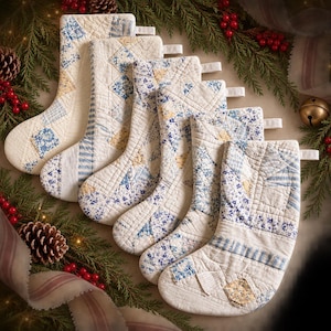 May include: A set of six quilted Christmas stockings featuring a patchwork design in shades of cream, light blue, and soft yellow. Each stocking is constructed from various fabric squares with floral and striped patterns and includes a hanging loop.