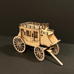 May include: A wooden stagecoach model with intricate details, including spoked wheels, a roof rack, and the words "HOLIDAY OVERLAND MAIL AND EXPRESS" etched on the side. The model is made of light-colored wood and sits against a dark background.
