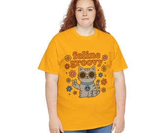 May include: Mustard yellow t-shirt with the words "feline groovy" above a cartoon cat wearing sunglasses and giving a peace sign. The cat is surrounded by colorful flowers. The shirt is made of a soft material.