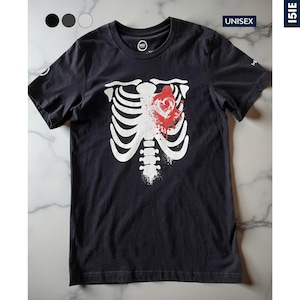 Può includere: T-shirt unisex grigio scuro con un design a gabbia toracica bianca e un cuore rosso. La maglietta ha maniche corte e girocollo. La parola "UNISEX" è stampata sulla maglietta. La maglietta è esposta su una superficie di marmo.