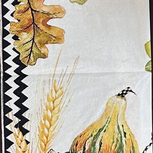 May include: A paper napkin featuring a black and white chevron border. The design includes watercolor illustrations of brown acorns, green and yellow oak leaves, golden wheat stalks, green succulents, and two gourds with black and white checkered stems.