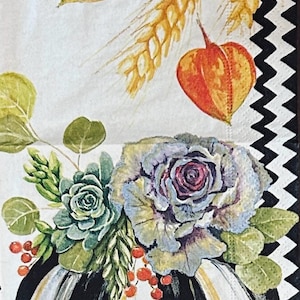 May include: A paper napkin featuring a black and white chevron border and a central illustration of a black and white striped pumpkin topped with a succulent, cabbage, red berries, wheat stalks, and orange physalis with MacKenzie-Childs text.
