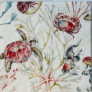 May include: Square white paper napkin with a watercolor design of sea creatures. The design includes a red sea turtle, crab, starfish, and fish, with coral and seaweed accents. The napkin has a textured surface.