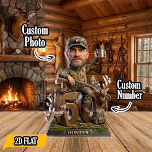 Peut inclure: Figurine d'un chasseur tenant un fusil et une tasse, assis sur un grand chiffre 50. La base indique "HUNTER". La figurine est placée dans un cadre de cabane rustique avec une cheminée et des bois de cerf. Le texte sur l'image indique "Custom Photo", "Custom Number" et "2D FLAT".