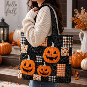Op de afbeelding: Een gewatteerde tas met een patchworkontwerp met oranje pompoenen, zwart-wit geblokte vierkanten en zwarte stof met witte vleermuisomtrekken. De tas heeft twee zwarte schouderbanden en een rechthoekige vorm.