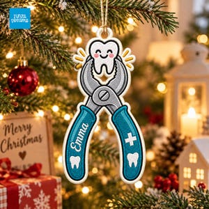 May include: A white embroidered Christmas ornament shaped like a pair of teal dental pliers holding a smiling white tooth. The handle features the name Emma in white script, a white tooth icon, and a white medical cross symbol on the other side.