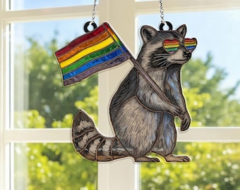 May include: A window decoration of a raccoon holding a rainbow flag and wearing rainbow heart-shaped sunglasses. The raccoon is grey and white with a striped tail. The flag has horizontal stripes of red, orange, yellow, green, blue, and purple.