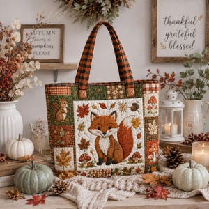May include: A quilted tote bag featuring a central panel with a cartoon fox, surrounded by autumn leaves and mushrooms. The bag has orange and black buffalo plaid handles and side panels with patchwork patterns of squirrels and forest motifs.