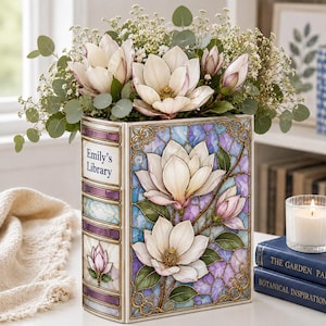 May include: A rectangular vase shaped like a book with the text Emily's Library on the spine. The vase features a stained glass pattern of white magnolia flowers against a purple and blue background, filled with fresh white magnolia flowers.