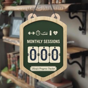 May include: A wooden sign with a dark green background and a light wood frame. The sign reads "MONTHLY SESSIONS" and has a counter showing "000". The top of the sign has fitness icons. The bottom of the sign reads "Olivia's Progress Tracker".