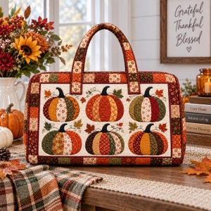 Op de afbeelding: Een rechthoekige gewatteerde tas met een patchwork rand in tinten oranje, bruin en groen. Het middenpaneel toont zes geappliqueerde pompoenen in diverse herfstachtige bloemen- en geometrische stoffen patronen met donkere steeltjes.