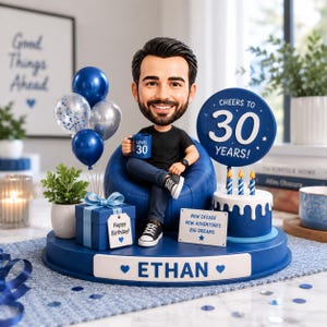May include: A custom bobblehead figure of a man with a beard sitting in a blue beanbag chair on a circular base. The base features the name ETHAN, a blue gift box labeled Happy Birthday, a cake with three candles, and a sign reading CHEERS TO 30 YEARS!