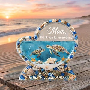 May include: Heart-shaped decorative piece with a beach theme. It features two sea turtles swimming in blue liquid, surrounded by seashells and starfish. The text reads "Mom, Thank you for everything" and "I love you To the Beach and Back."