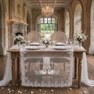May include: A rectangular wooden dining table set for two with a white lace table runner featuring the text The Williams, an illustration of two swans forming a heart, and Est. 2026. The table includes white plates, glassware, and floral centerpieces.