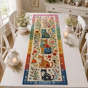 May include: A rectangular fabric table runner featuring a vertical arrangement of five illustrated cats surrounded by seasonal floral and botanical motifs, including sunflowers, tulips, pumpkins, mushrooms, and snowflakes, with a colorful gradient border.