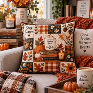 May include: A square quilted throw pillow featuring a patchwork design with autumn-themed illustrations including pumpkins, fall leaves, daisies, and a mug with the text Pumpkin Spice & Good Books, stacked on books labeled Fall Stories, Cozy Days, and Brighter Nights.