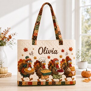 May include: A quilted tote bag with a cream background featuring the name Olivia in brown script. The design includes four cartoon turkeys carrying Thanksgiving food items, surrounded by small orange and red maple leaves and stars.