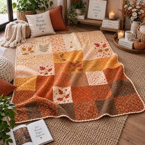 May include: A patchwork quilt featuring a variety of square fabric blocks in shades of orange, yellow, brown, and cream. The quilt displays repeating patterns of autumn leaves, small floral prints, and textured stitching throughout the design.