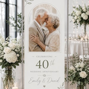 May include: A vertical banner on a metal stand featuring a photo of an older couple embracing inside an arched frame. Text reads: CELEBRATING 40th WEDDING ANNIVERSARY, Emily & David, and MARCH 14, 1985. The design includes green leaf illustrations.