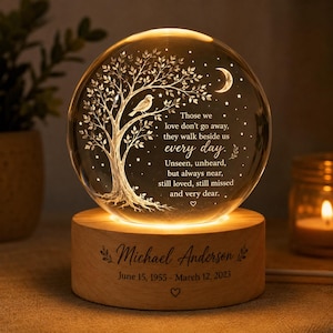 May include: A spherical glass night light featuring an etched tree, a bird, a crescent moon, and stars. The text reads: Those we love don't go away, they walk beside us every day. Unseen, unheard, but always near, still loved, still missed and very dear. The wooden base is engraved with Michael Anderson, June 15, 1955 - March 12, 2023.