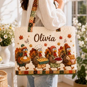 May include: A quilted tote bag featuring the name Olivia in brown script, decorated with four cartoon turkeys carrying Thanksgiving dishes, including a pie, casserole, bowl of cranberries, and bread rolls, accented by scattered autumn leaves.