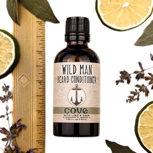 Wild Man Beard Oil Conditioner Cove scent in 50ml amber glass bottle. Shown next to ruler at about 4" tall. Lime slices and sage leaves surround.