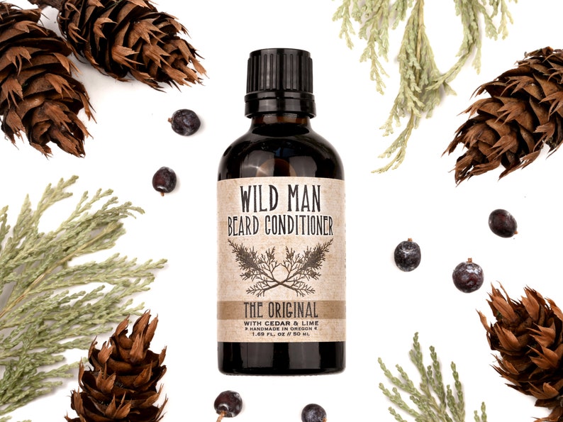 Wild Man Beard Conditioner in The Original scent shown in a 50ml amber glass bottle. Cedar, fir cones and juniper berries surround.