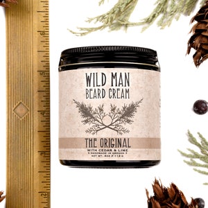 Wild Man Beard Cream in The Original scent shown in a 4oz amber glass jar. Shown next to a ruler at about 3" tall. Cedar, fir cones and juniper berries surround.