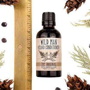 Wild Man Beard Conditioner in The Original scent shown in a 50ml amber glass bottle. Shown next to ruler measuring about 4" tall. Cedar, fir cones and juniper berries surround.