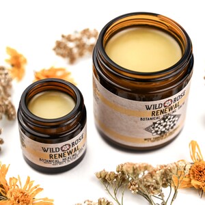 Renewal Healing Salve in a amber glass jars. Lids are removed revealing a creamy yellow balm. Dried yarrow and calendula surround.