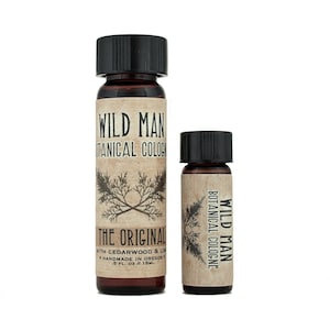 May include: Two amber glass bottles of Wild Man Botanical Cologne with black screw caps. The larger bottle label reads Wild Man Botanical Cologne, The Original, with Cedarwood & Lime, Handmade in Oregon, .5 fl. oz / 15ml. The smaller bottle label reads Wild Man Botanical Cologne.